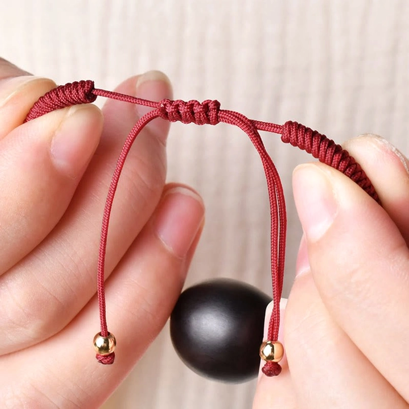 Close-up of red woven cord cat bracelet with gold tone hardware and detachable bead