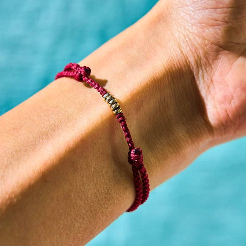 Woven red cord bracelet with silver beads on wrist showing adjustable knot detail