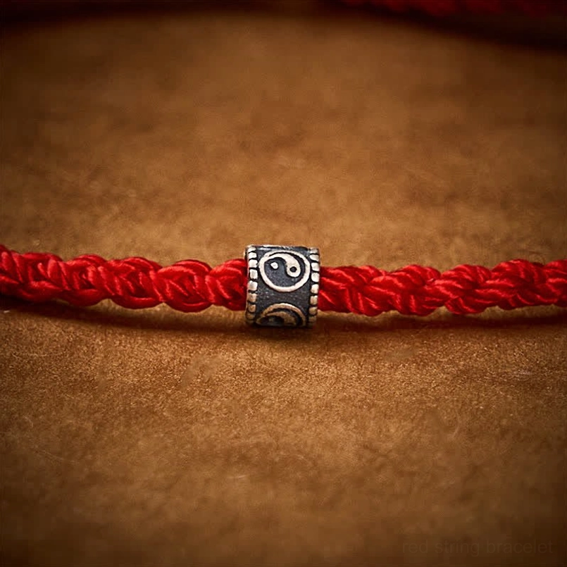 Macro close-up of red braided cord and silver Yin Yang bead texture detail