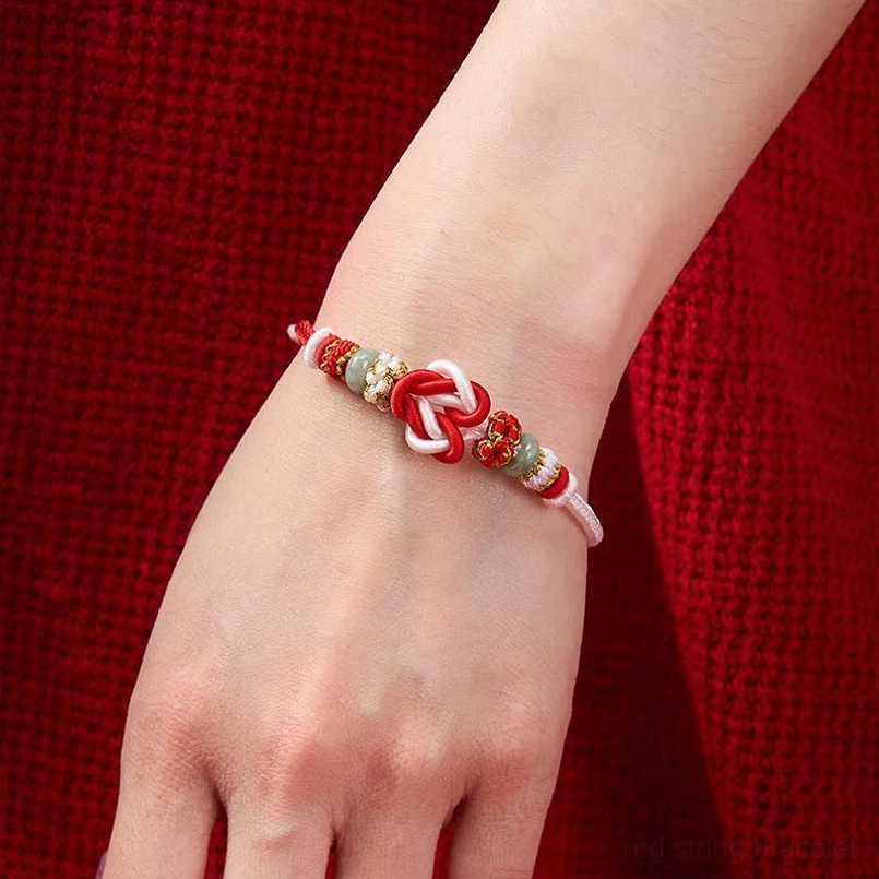 Red gold jade heart knot bracelet displayed on wooden bowl styling