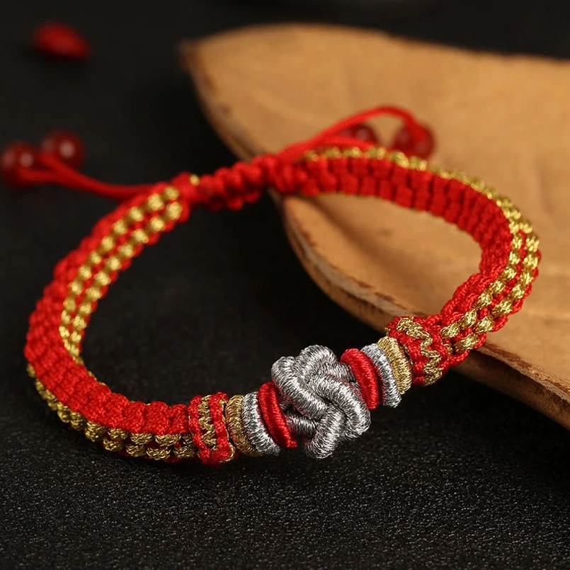 Red gold handmade lucky braided bracelet with silver Chinese knot on wooden display stand