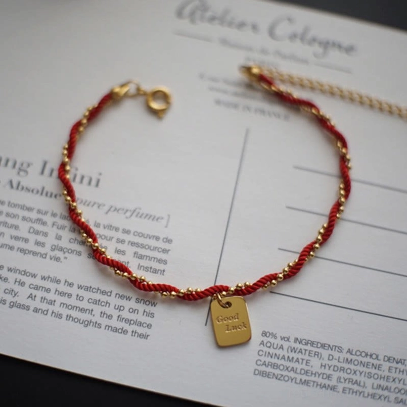 Red gold woven cord bracelet side overhead view with Good Luck charm detail