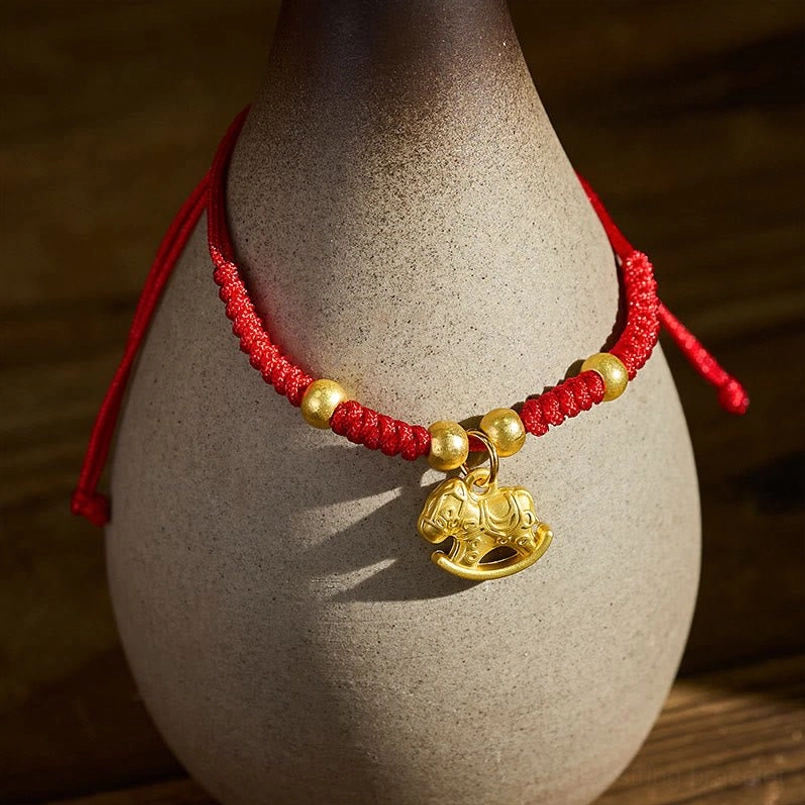 Red string horse charm bracelet displayed on ceramic vase, showing matte gold tone accents and adjustable red cord