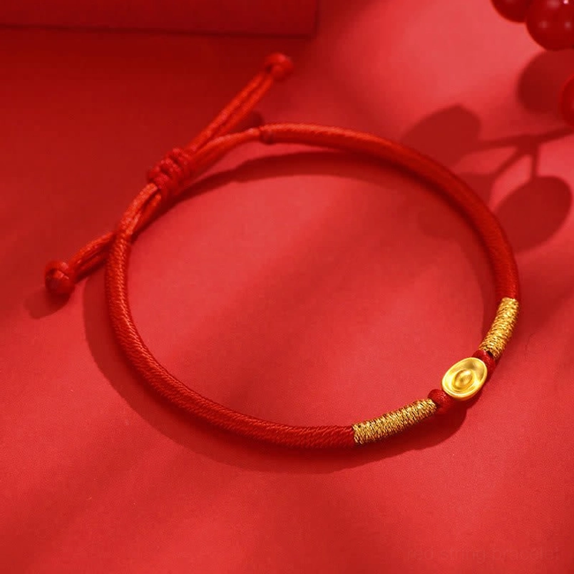 Flat lay of red braided string bracelet with gold thread wrapping and gold ingot charm