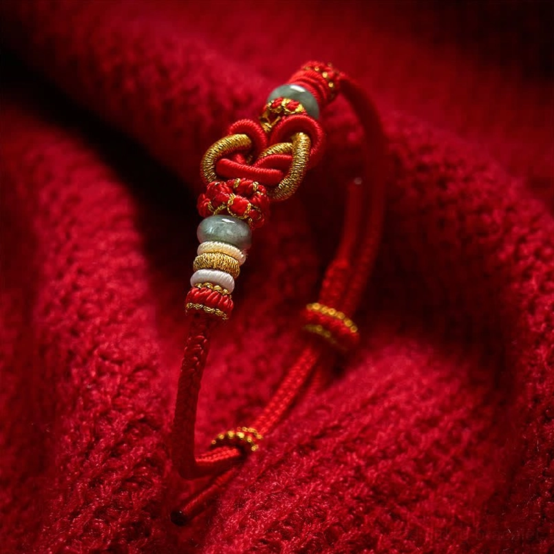 Red woven bracelet with heart knot design and jade bead accents close-up