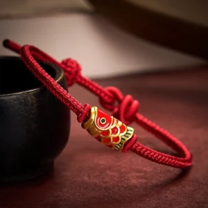 Red koi fish braided string bracelet with gold-red enamel charm, adjustable cord knot, close-up three-quarter view