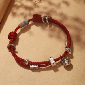 Red braided string koi fish silver bracelet with engraved charm on wooden surface