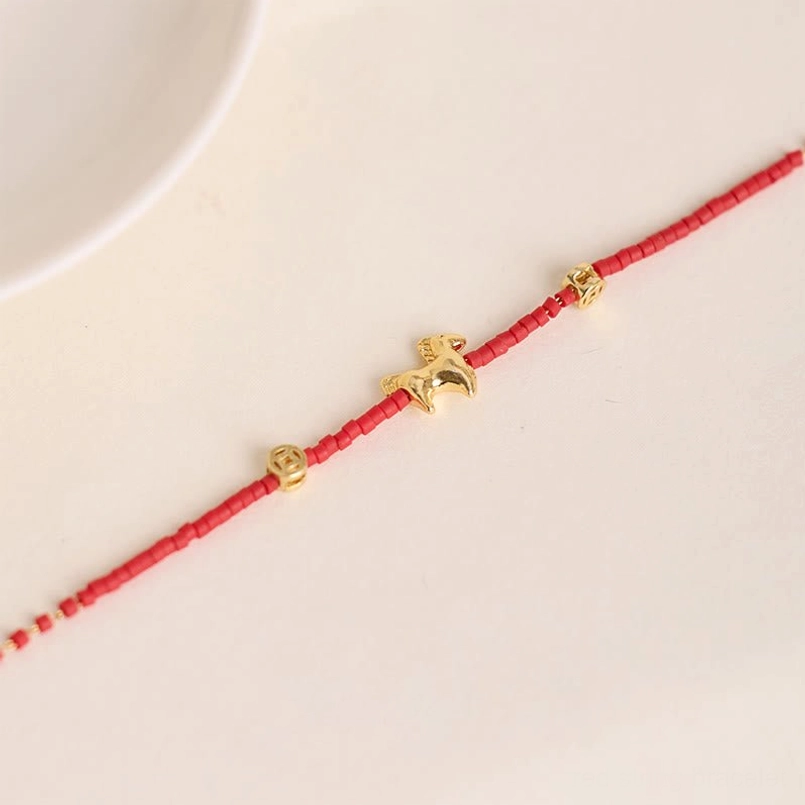 Close-up side view of red liuli glass beads with gold horse and coin accents on white plate