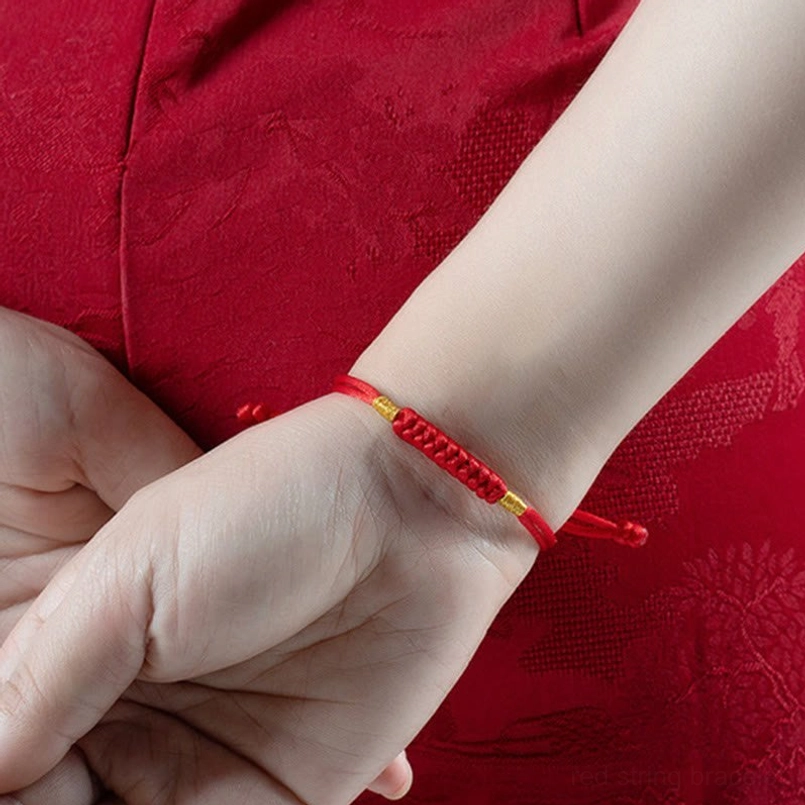 Red string lucky knot bracelet worn on wrist with traditional red embroidered clothing backdrop