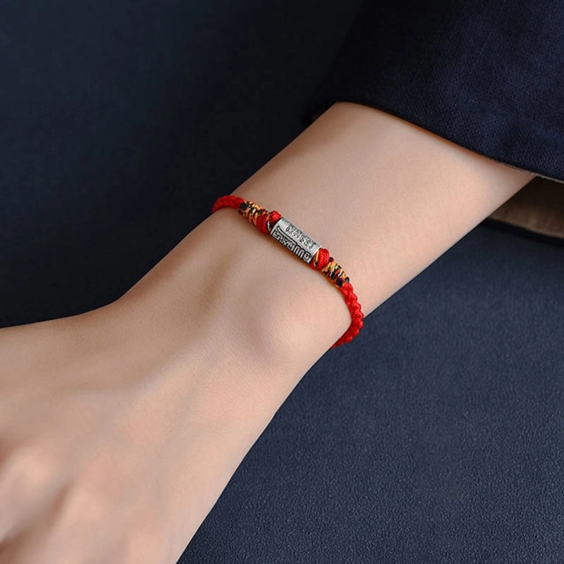 Slim red woven lucky bracelet on wrist with engraved sterling silver charm worn view