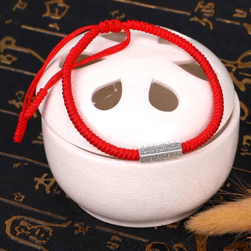 Red string Tibetan mantra bracelet side view with engraved silver charm and adjustable sliding knot