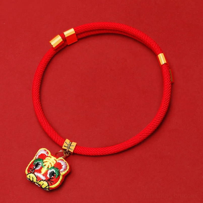 Red pet collar with gold hardware and upside-down tiger head pendant overhead flat lay