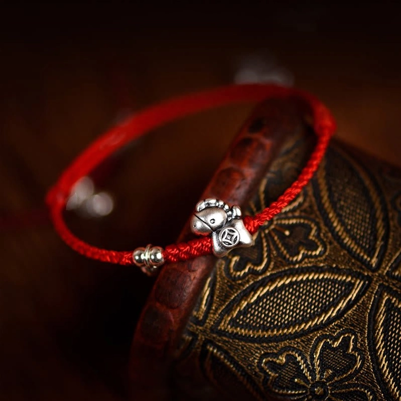 Braided red rope with silver horse coin charm and metal securing beads low-angle side view