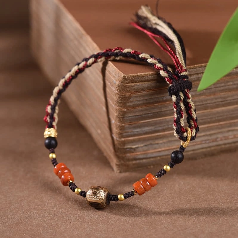 Hand-woven red sandalwood protection bracelet with multicolor cord tassel and decorative metal barrel bead on wooden box