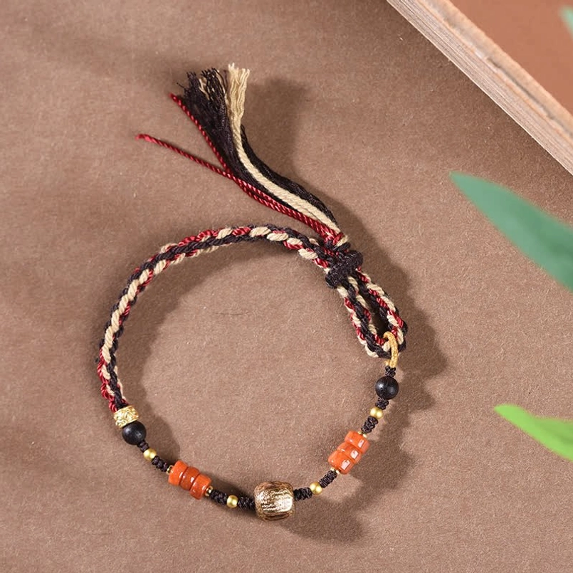 Delicate hand-woven red sandalwood protection bracelet with multicolor tassel and complete bead set against green leaf background