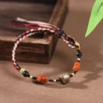 Red sandalwood hand-woven blessing bracelet with protection cord, multicolor braided design with agate beads and metal accents on wooden tray