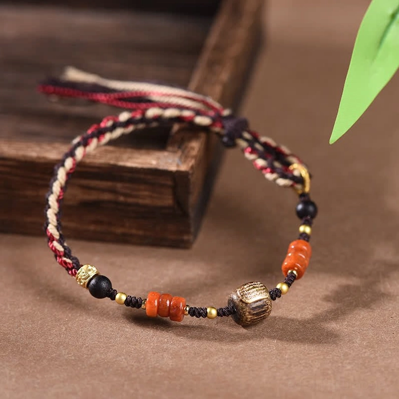 Red sandalwood hand-woven blessing bracelet with protection cord, multicolor braided design with agate beads and metal accents on wooden tray