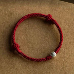 Red woven fortune bracelet with 925 sterling silver Fu charm flat lay on brown fabric background