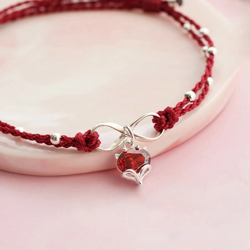 Close-up detail of red braided string anklet showing silver beads, heart pendant, and infinity clasp