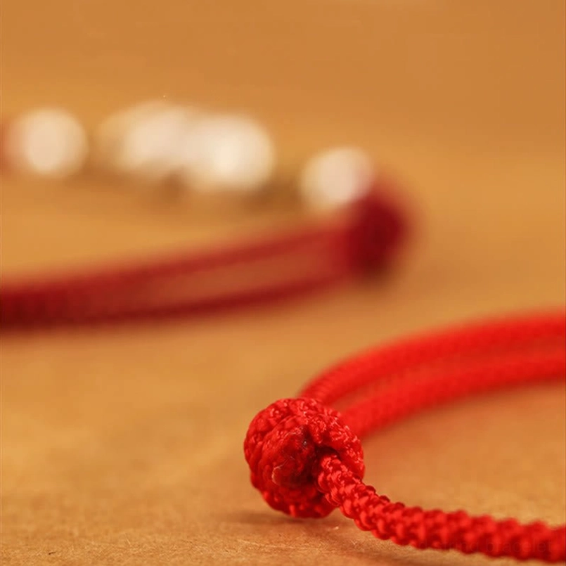 Macro detail view of red string ankle bracelet showing braided knot end and woven red cord with silver bead accents