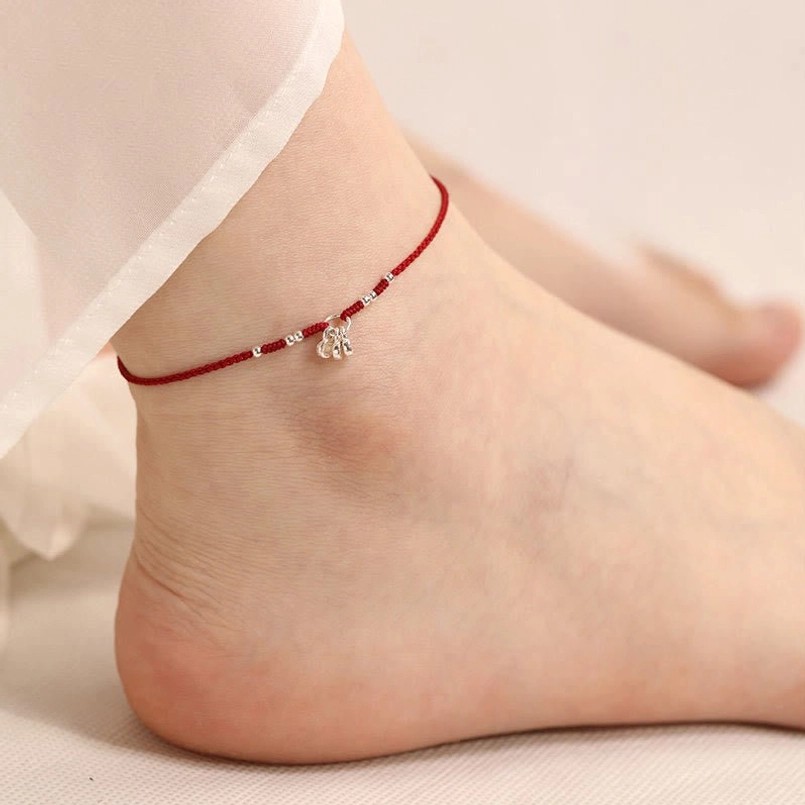 Red string ankle bracelet worn on ankle showing hanging fortune charms and silver bead details