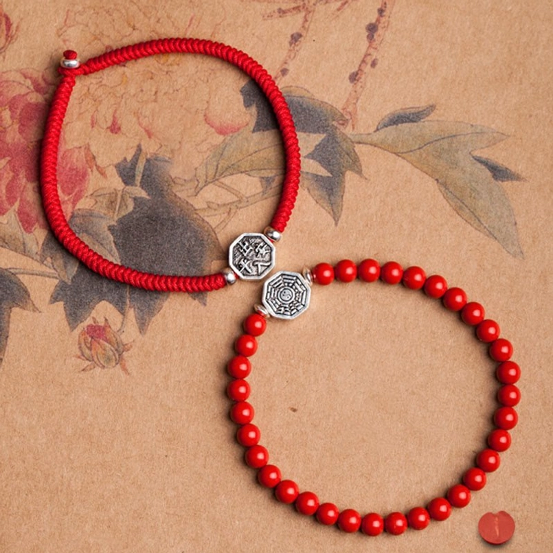 Red string bracelets with bagua charm and cinnabar beads on floral background