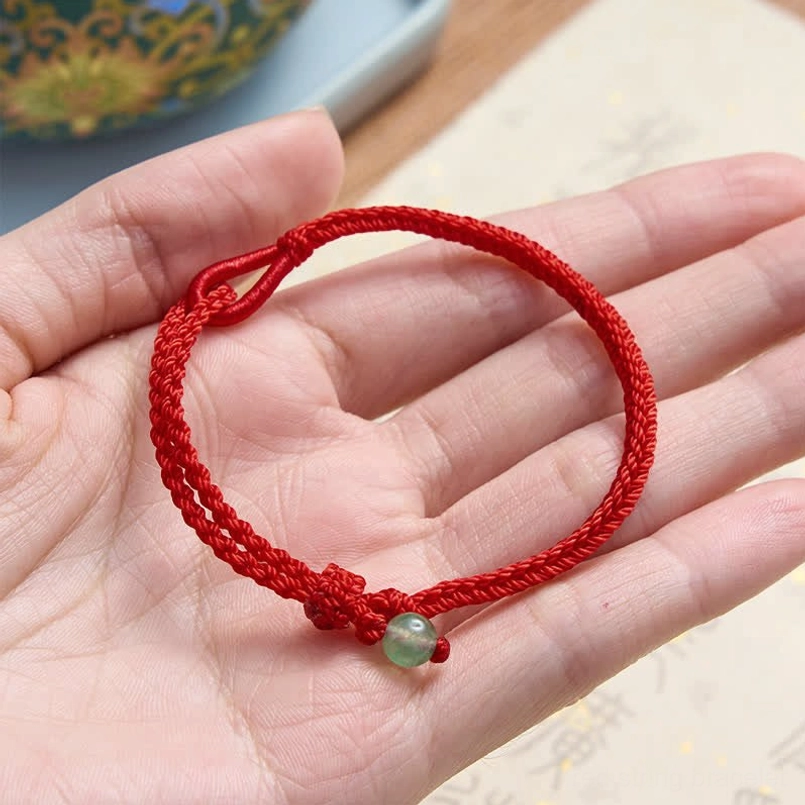 Red string balance bracelet lying on palm with green aventurine bead and adjustable loop clasp