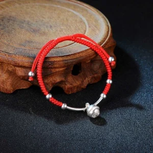 Red string bell bracelet with silver charms on wooden display stand