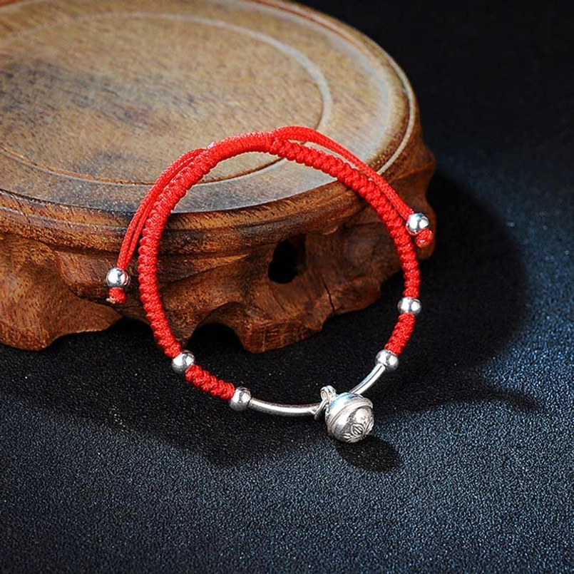 Red string bell bracelet with silver charms on wooden display stand