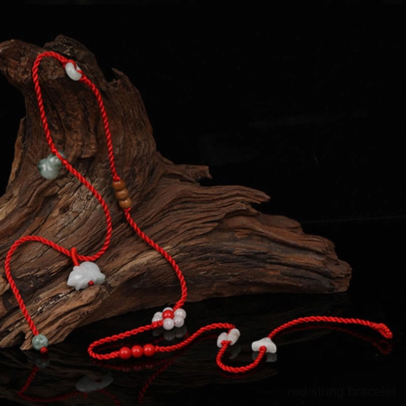 Red string belly chain with woven cord and jade beads on dark aged wood background - close-up