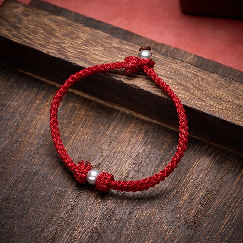 Red braided red string bracelet with 925 silver beads side view on dark wooden plank