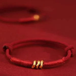 999 gold bead red string bracelet with three twisted gold rings on burgundy background