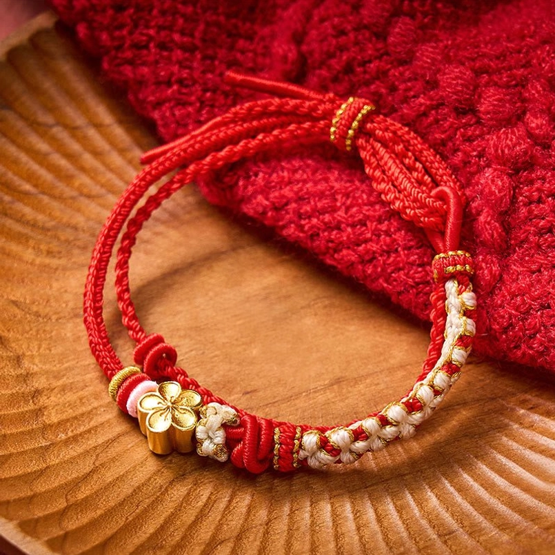 Red woven destiny bracelet with gold flower charm side view on wooden coaster