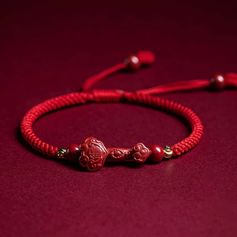 Adjustable red string bracelet with multiple cinnabar charms and pull-cord closure, overhead view