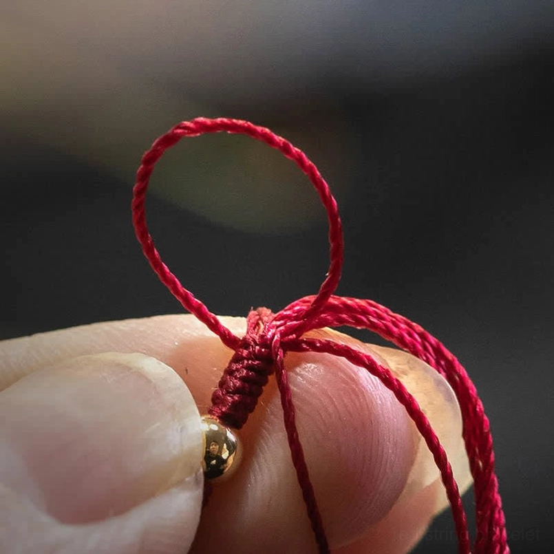 Extreme close-up of braided red string bracelet adjustment knot with metal bead, demonstrating pull-to-adjust mechanism