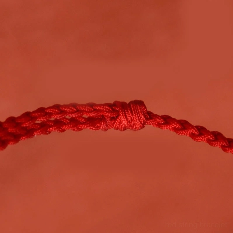 Red string bracelet adjustable fastening knot macro view on red fabric background