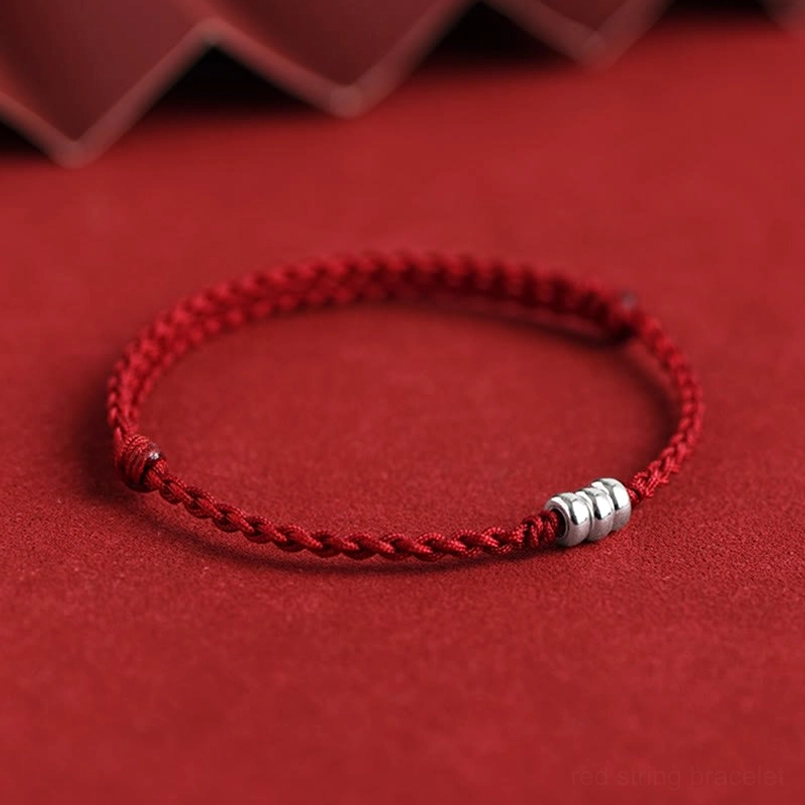 Red braided silver bead bracelet with knotted cord ends on fabric with geometric trim