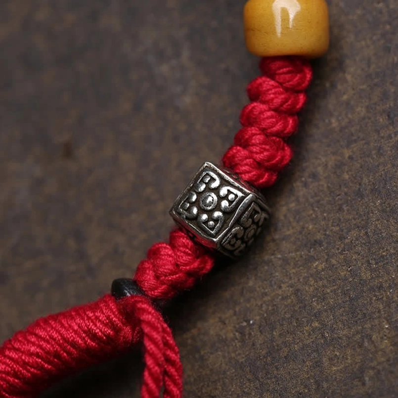 Close-up of red braided cord knot and carved Buddha bead detail