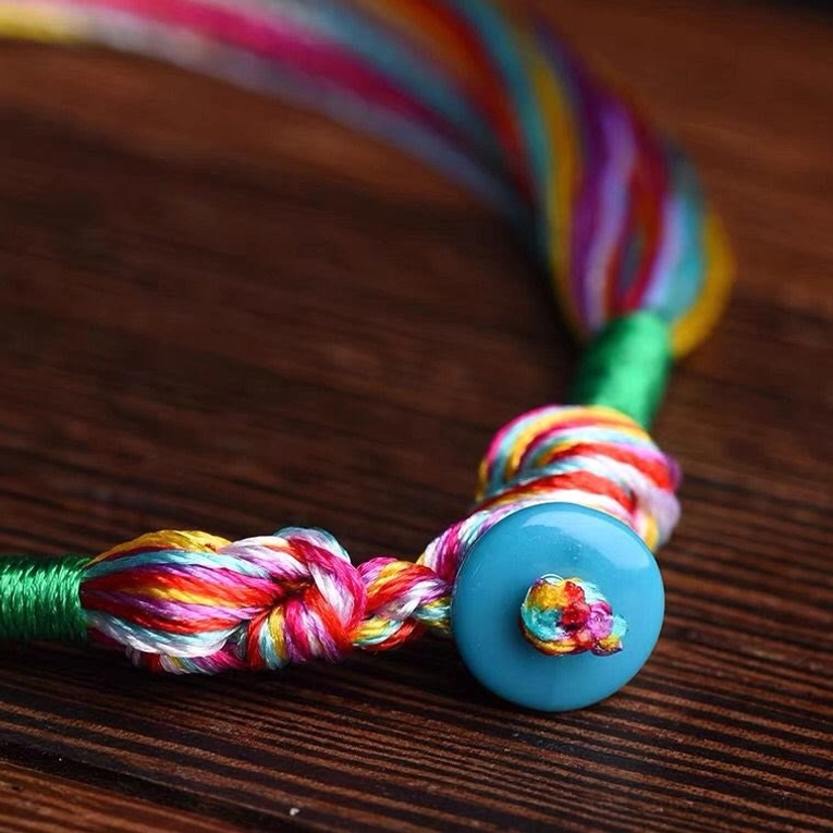 Red string bracelet braided knot and blue charm fastening detail close up