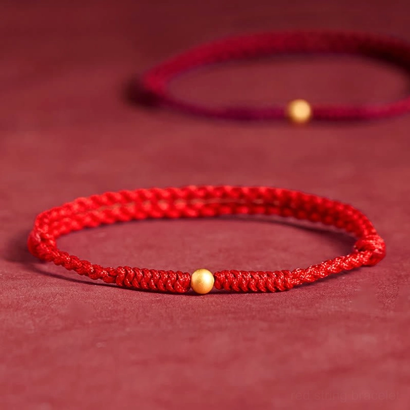 Bright red string bracelet with prominent gold bead, vibrant color close-up