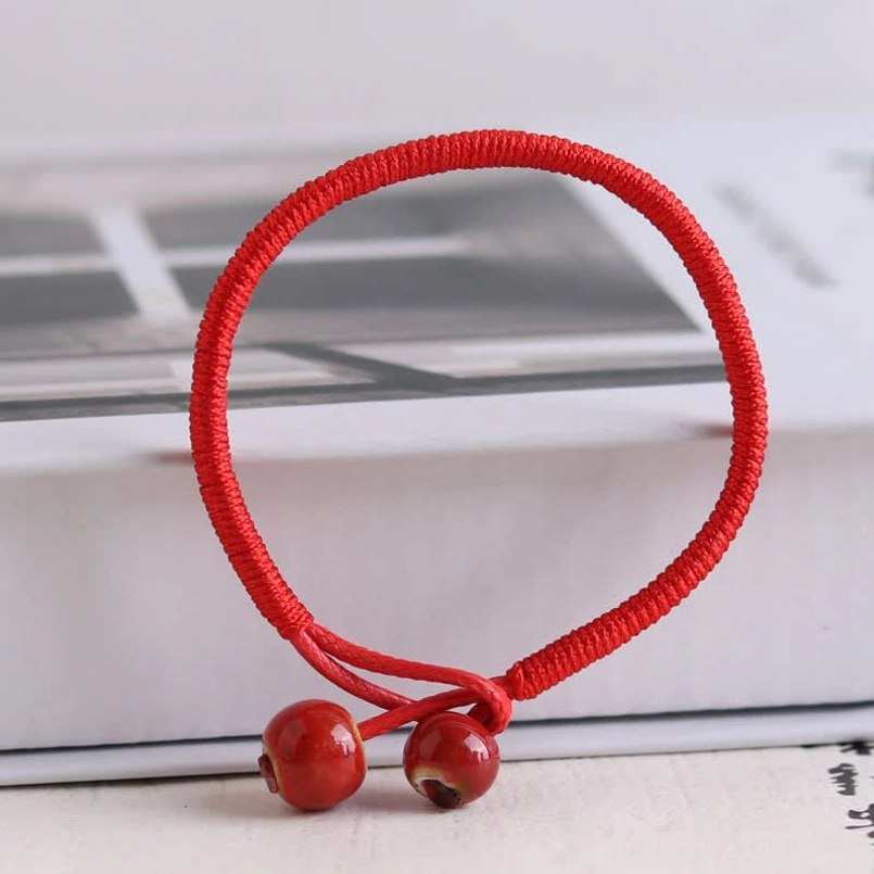 Front close-up of red string ceramic bracelet with dangling ceramic beads on knot closure