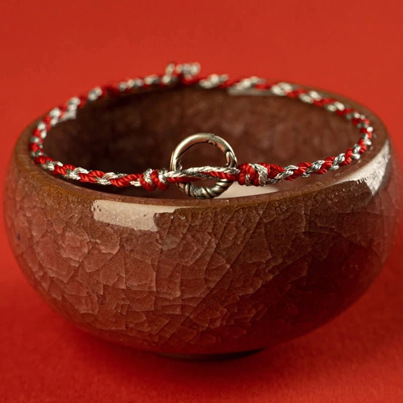 Luck string bracelet with red-silver braided rope on crackled ceramic bowl