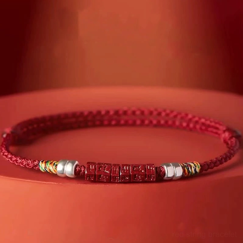 Tibetan red string bracelet with engraved cinnabar mantra bead, studio photography on red platform