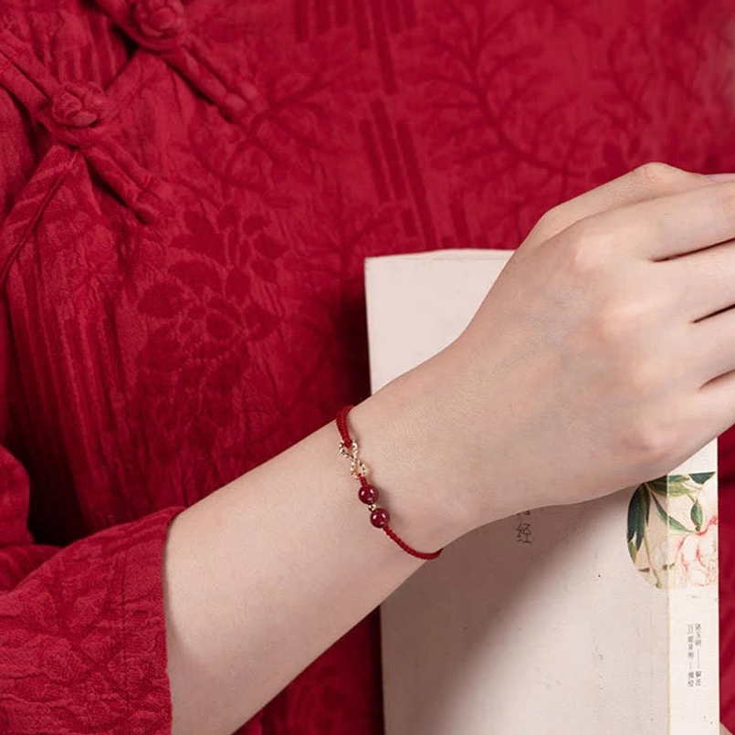 Premium red string infinity bracelet on wrist with cinnabar beads and gold accents, close-up side view