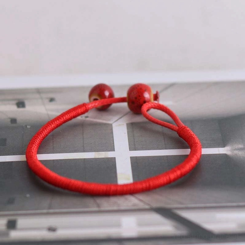 Front flat lay circular view of red string bracelet with ceramic bead closure on patterned background