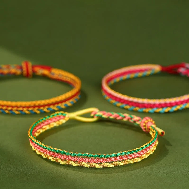 Collection of multiple handcrafted red string bracelets in various chakra color combinations laid out flat