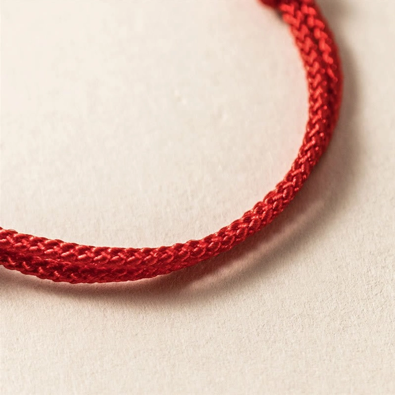 Plain braided red cord string bracelet without charm showing woven texture detail