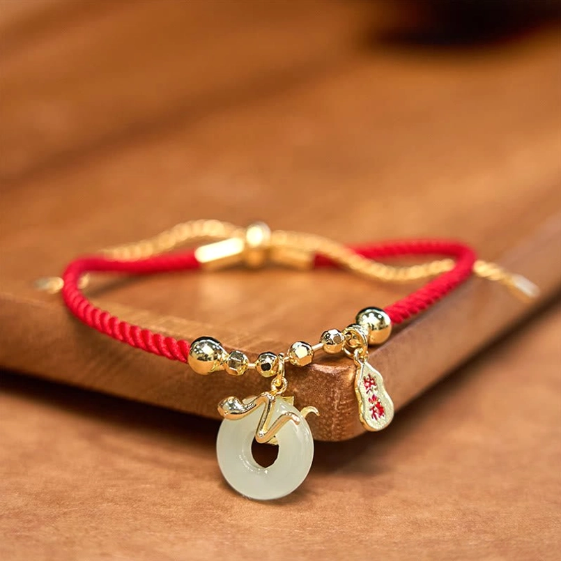 Red string bracelet with dangling jade peace buckle charm and gold hardware detail