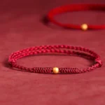 Dark red braided string bracelet with gold accent bead, close-up on fabric