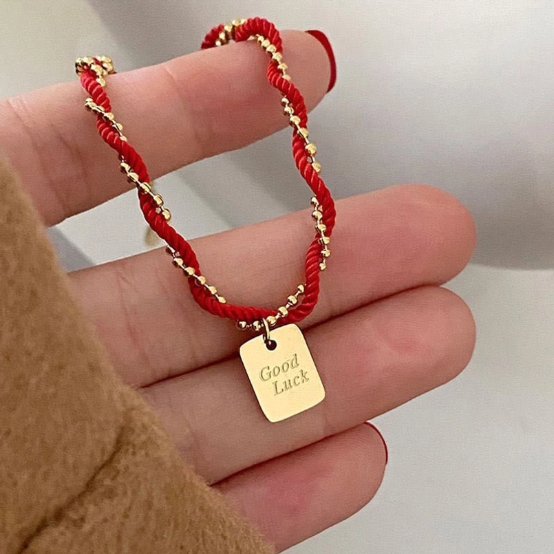Red string good luck bracelet close up detail shot of engraved copper charm